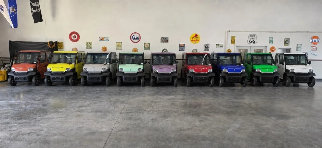 Atomic Coupe color lineup at the Wildwood showroom — Orange, Yellow, White, Mint, Purple, Red, Blue, Green, and White carts parked side by side